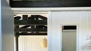 A room with a wooden floor, a dining table with chairs, a hanging light fixture, and a white door with a small mirror. - Summer house vibe at Kandestederne (Skagen)