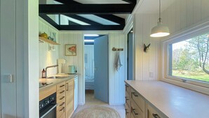 A modern kitchen with wooden cabinets, a built-in oven, and a large window. - Summer house vibe at Kandestederne (Skagen)