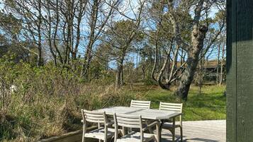 A wooden deck with a table and chairs, surrounded by trees and a clear sky.
