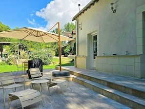 Une terrasse extérieure avec des chaises et une table en métal, un espace couvert avec une table et des chaises, et un bâtiment dont l’extérieur est revêtu de carreaux.