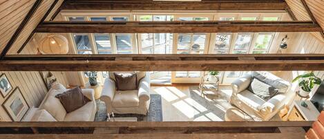A high-ceilinged room with a sloped roof, large windows, and a view of the outdoors.