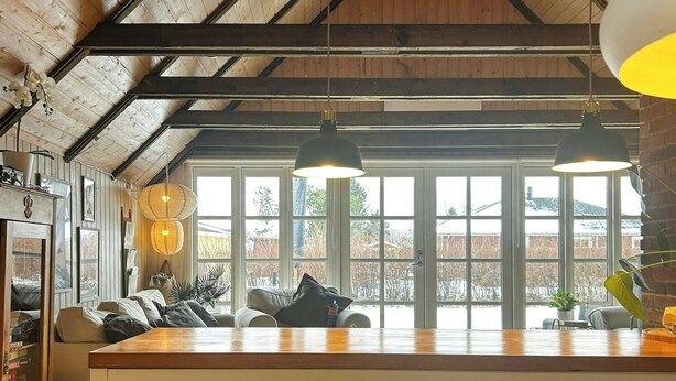 A kitchen with a wooden ceiling, large windows, and a central island with chairs.