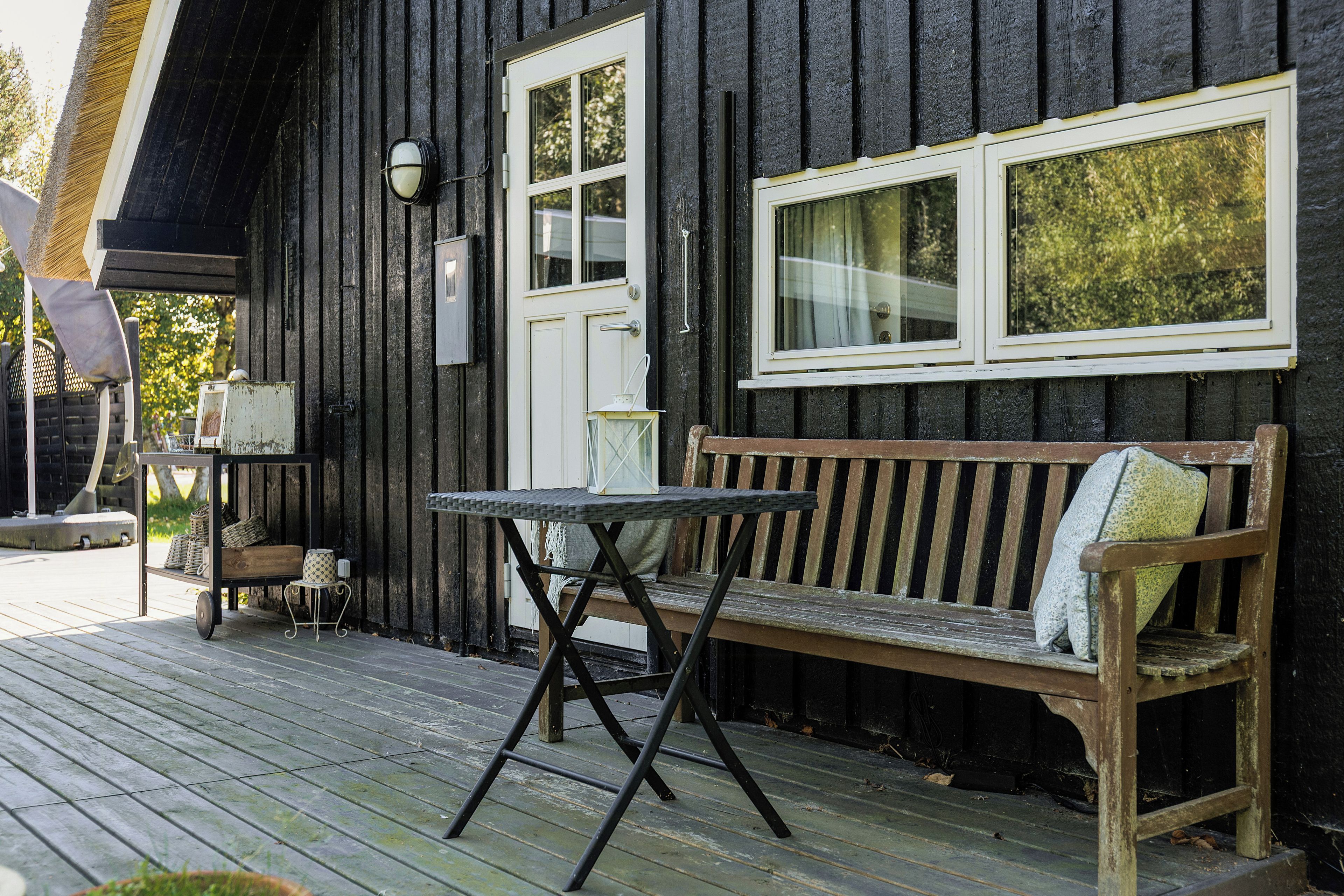A wooden bench with cushions, a small table, and a door with windows on a wooden porch.