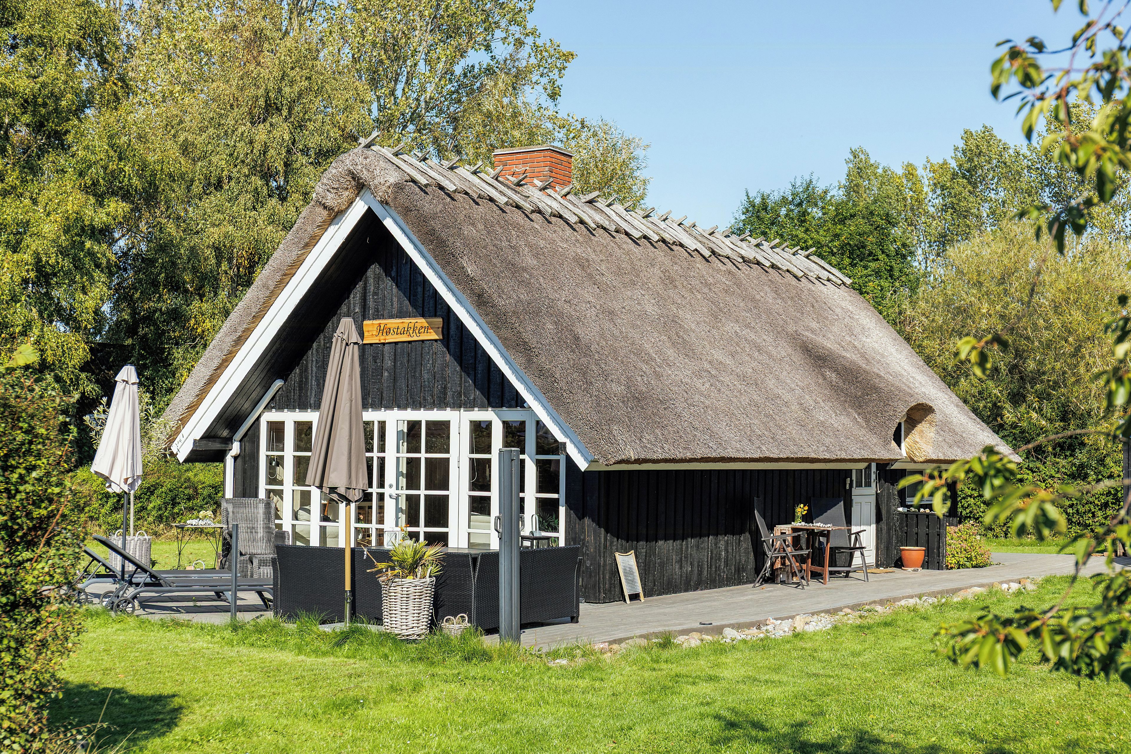 En traditionel bygning med stråtækt tag og et skilt, der siger 'Hostaken'.