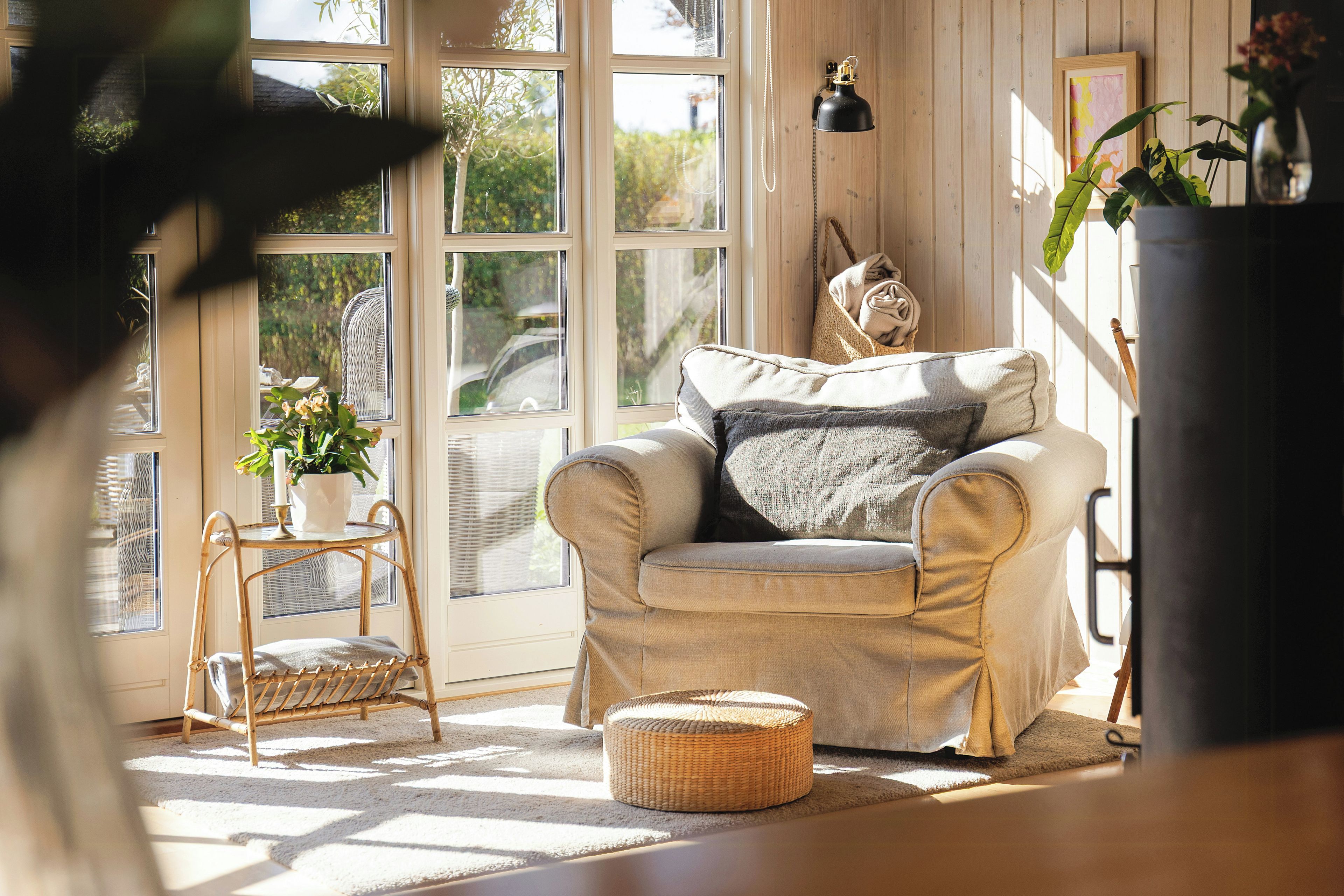 A cozy room with a beige sofa, a wicker chair, a small table with a candle, and a potted plant.