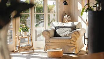 A cozy room with a beige sofa, a wicker chair, a small table with a candle, and a potted plant.