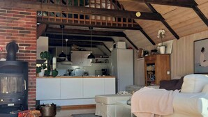 A cozy living room with a fireplace, a sofa, and a kitchen area in the background.