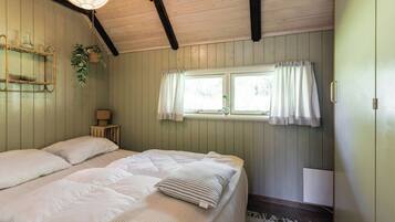 Una habitación con una cama, una ventana con cortinas, una lámpara de noche y un estante en la pared con una planta.