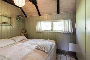 A room with a bed, a window with curtains, a bedside lamp, and a wall-mounted shelf with a plant. - Thatched cottage with wildlife near Kramnitze (Dannemare)