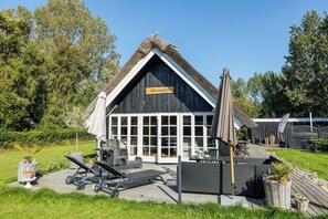Un bâtiment avec un toit de chaume, une enseigne indiquant « Hostaken », et un patio aménagé avec du mobilier d’extérieur.