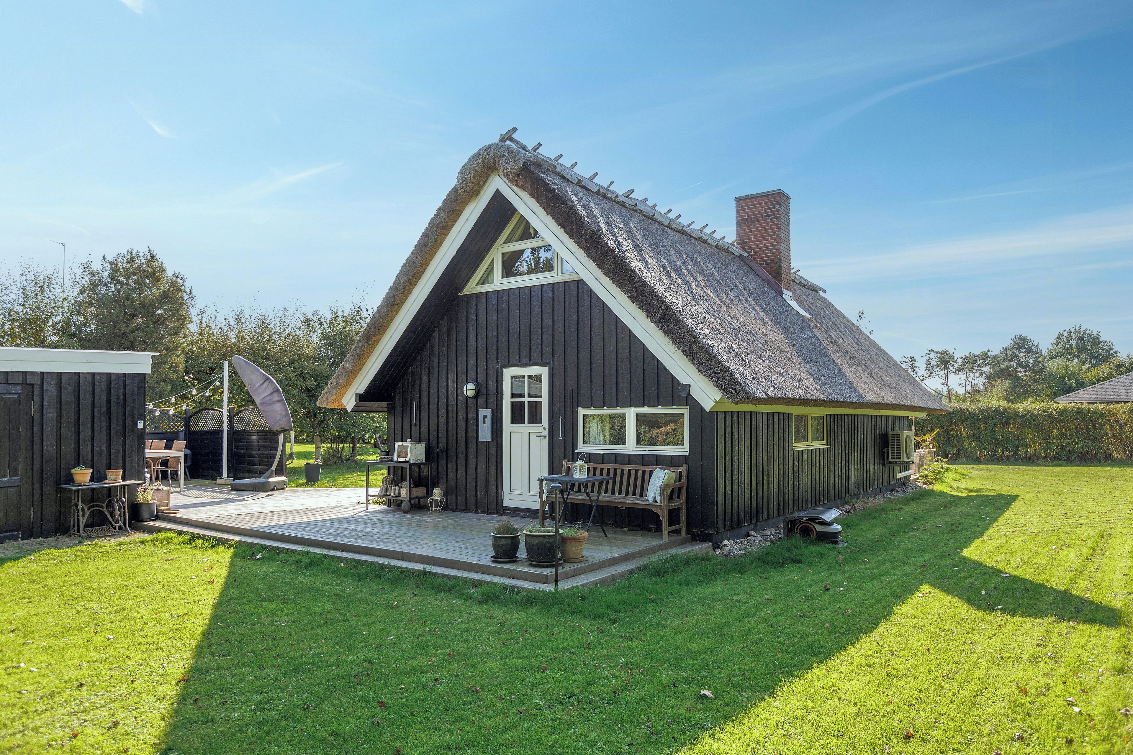 Et hus med et stejlt tag, en veranda med en bænk og et lille haveområde.