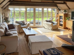 A spacious living room with a large sliding glass door leading to a garden, a sofa set, a coffee table, and a television.