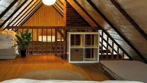 A bedroom with a sloped ceiling, a bed, a potted plant, and a white cabinet with baskets.