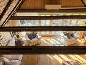 A room with a sloped ceiling, wooden beams, a ceiling fan, and a large window with multiple panes.