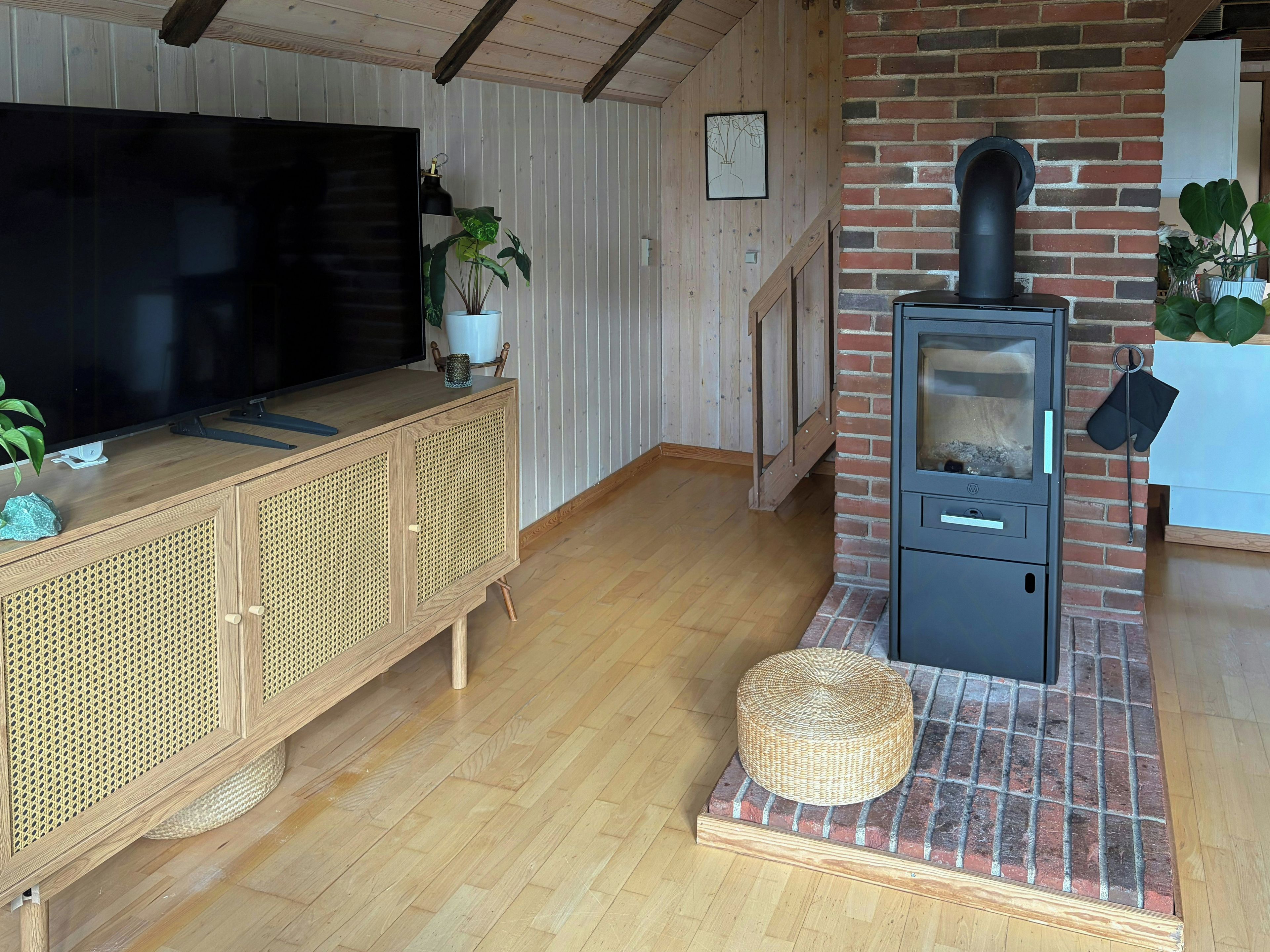 A living room with a television, wooden furniture, a brick fireplace, and a staircase.
