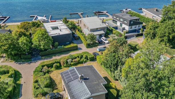 Vista aerea di una proprietà sul lago con case moderne, un porto turistico e una piccola isola.