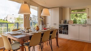 Una cucina moderna con mobili bianchi, un tavolo da pranzo per quattro persone e un'ampia finestra con vista su un paesaggio verde.