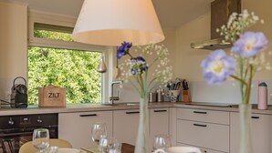 Una cucina moderna con zona pranzo apparecchiata per un pasto, una finestra con vista su piante e un bagaglio con l'etichetta 'ZILT VAKANTIES'.