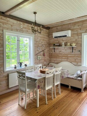 A cozy room with a dining table, chairs, a sofa, a chandelier, and a window with a view of greenery. - Historic dock house in the heart of Småland (Hult)