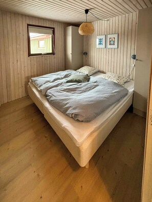 Un dormitorio con cama, paredes de madera, una ventana y cuadros en la pared.