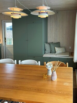 Un comedor con una mesa de madera, sillas, un banco con cojines e iluminación colgante.