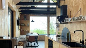 Een moderne keuken met houten kastjes, een inbouwoven en een groot raam met uitzicht op groen.