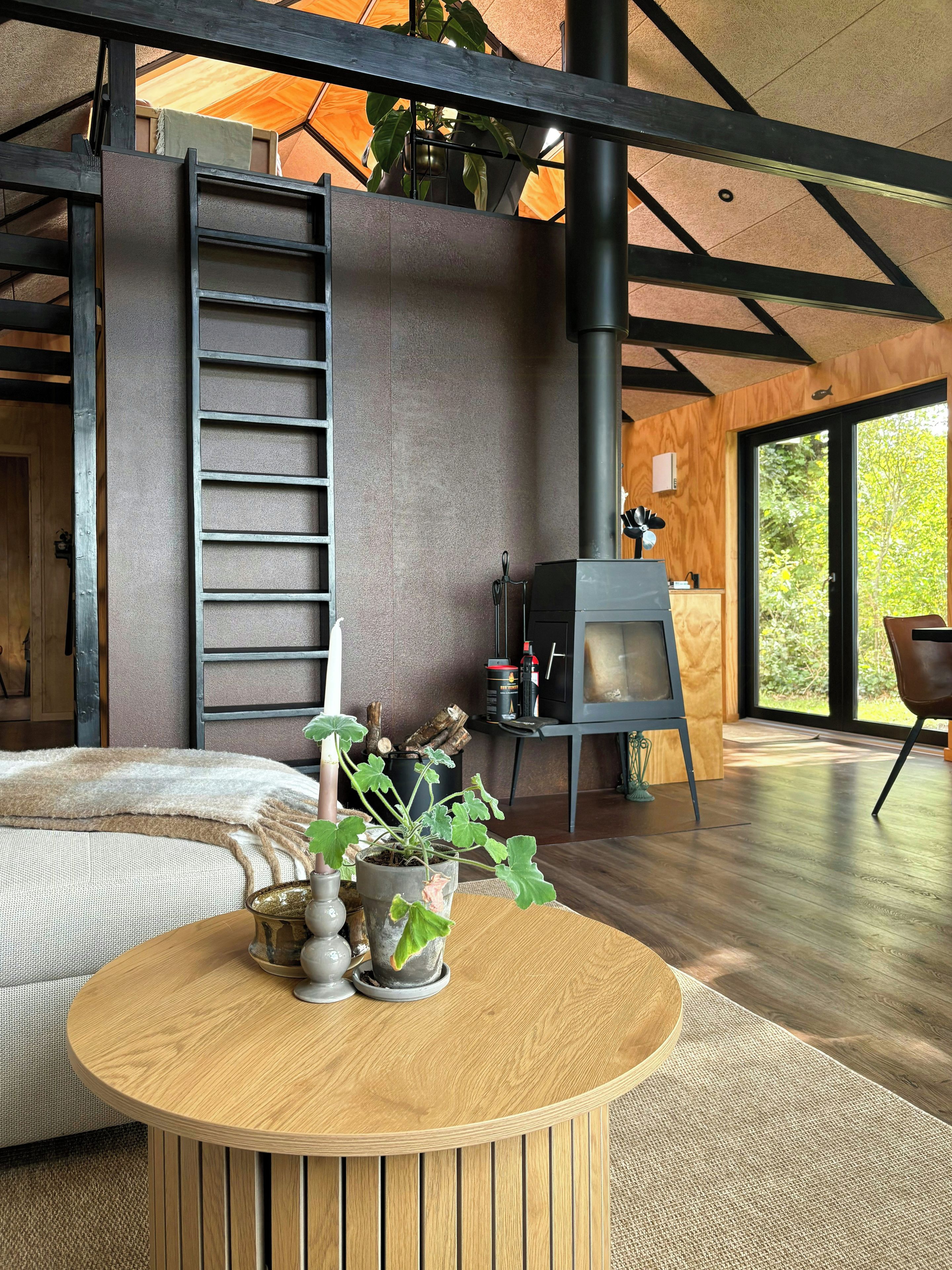 A modern interior with a central wooden table, a fireplace, and a large window.