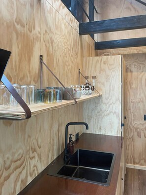 Eine kleine Küche mit Holzbeschichtung, einem schwarzen Spülbecken und einem Regal mit Gläsern und einem Wasserkocher.