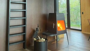 Een modern interieur met een houtkachel, een metalen ladder en een raam met uitzicht op groen.