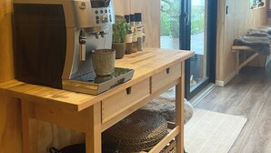 Een houten keuken met een koffieapparaat, planken met keukengerei en uitzicht op de omgeving.