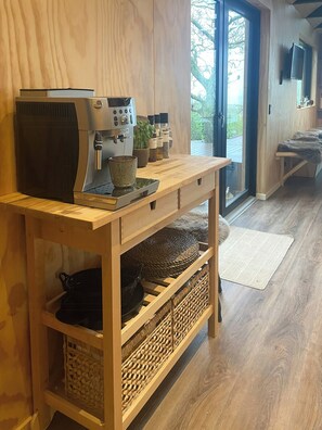 A wooden kitchen with a coffee machine, shelves with kitchenware, and a view of the outdoors. - Modern wooden house near Halkær bredning (nibe)