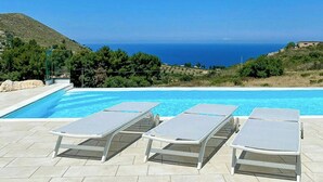 Una piscina amb gandules, cel serena i vista al mar i les muntanyes.