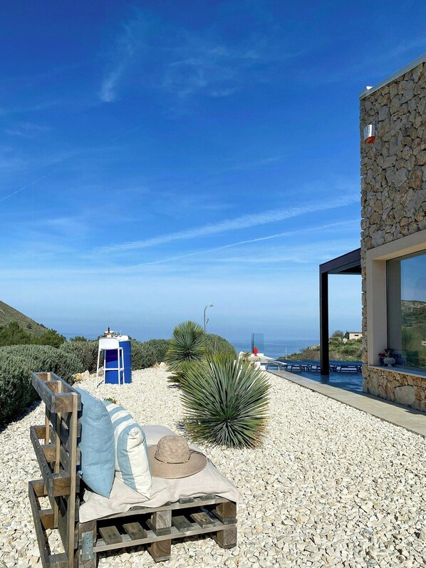 Eine Terrasse mit einer hölzernen Bank, einer blauen mobilen Toilette und einer großen Agavenpflanze.