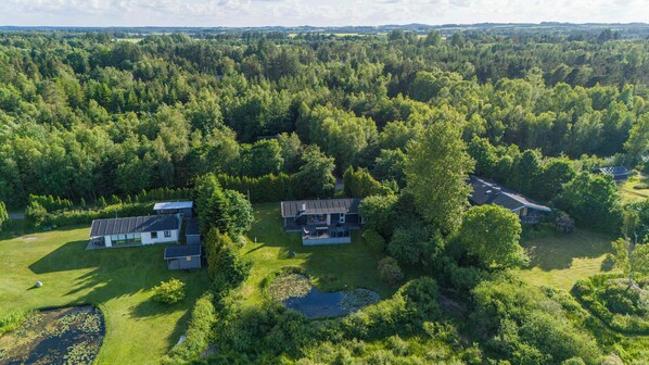 A large house surrounded by dense forest, with a pond and solar panels on the roof. - Panoramic view and terrace in charming home (Hojslev)