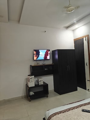 A bedroom with a bed, a TV mounted on the wall, a wardrobe, and a small table with boxes. - Hotel Yogasthali Rishikesh (Rishikesh)