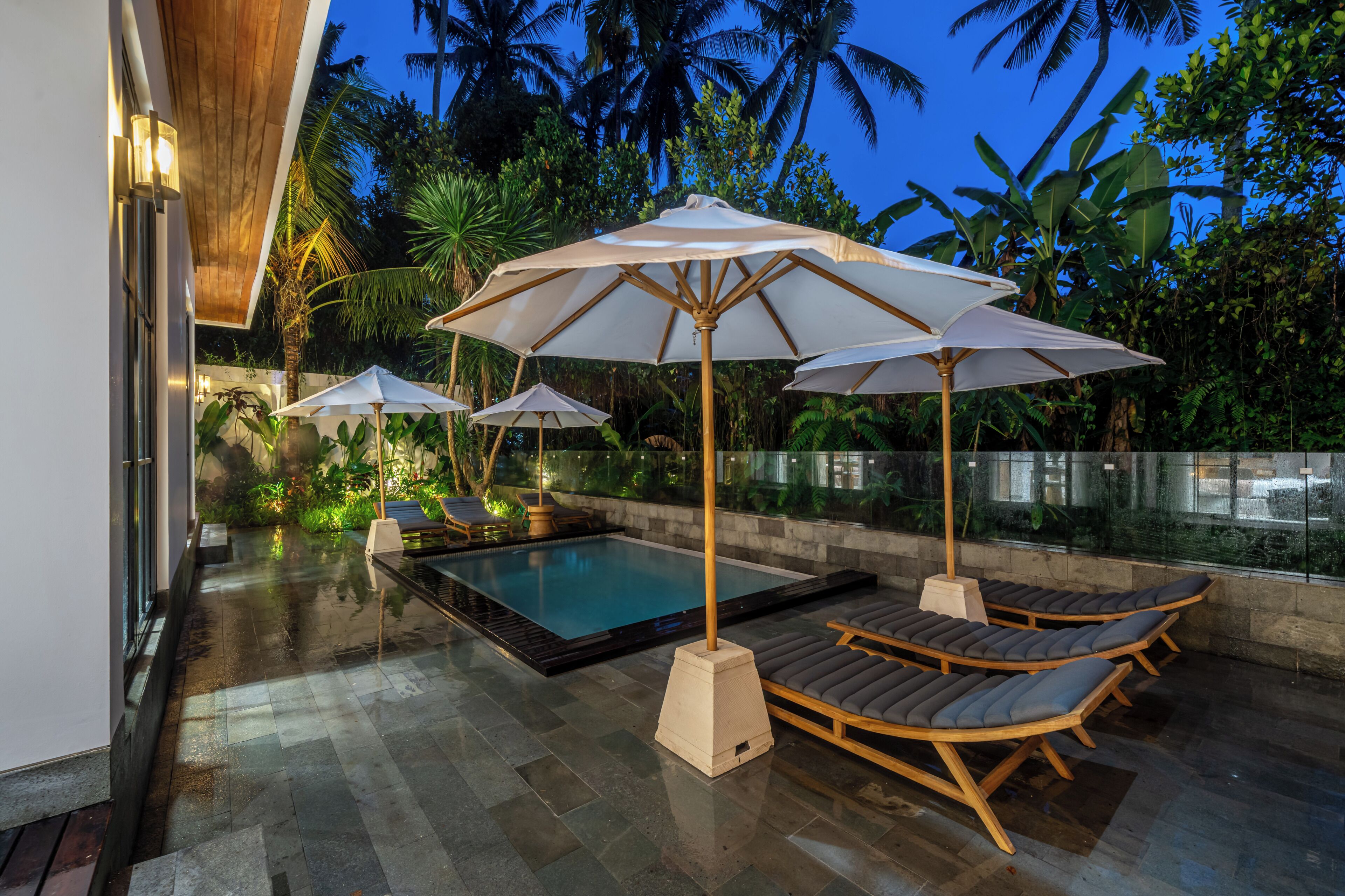 A poolside area with lounge chairs and umbrellas, surrounded by tropical vegetation.