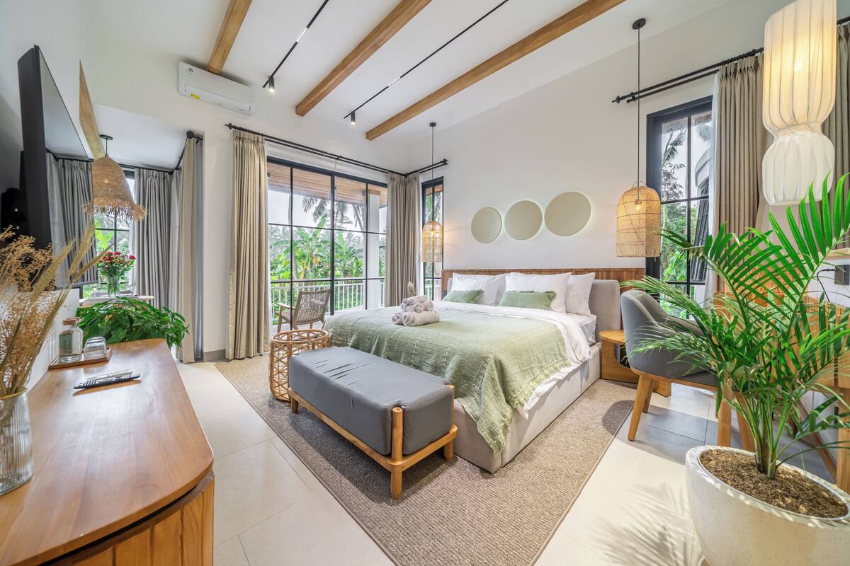 A modern bedroom with a bed, bedside table, chair, and potted plants.