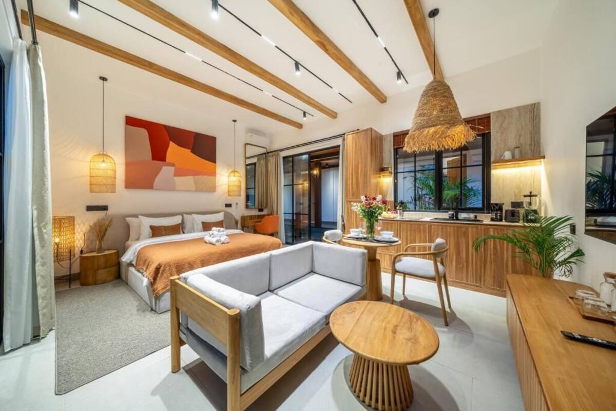 A modern hotel room with a bed, sofa, dining table, and kitchenette.