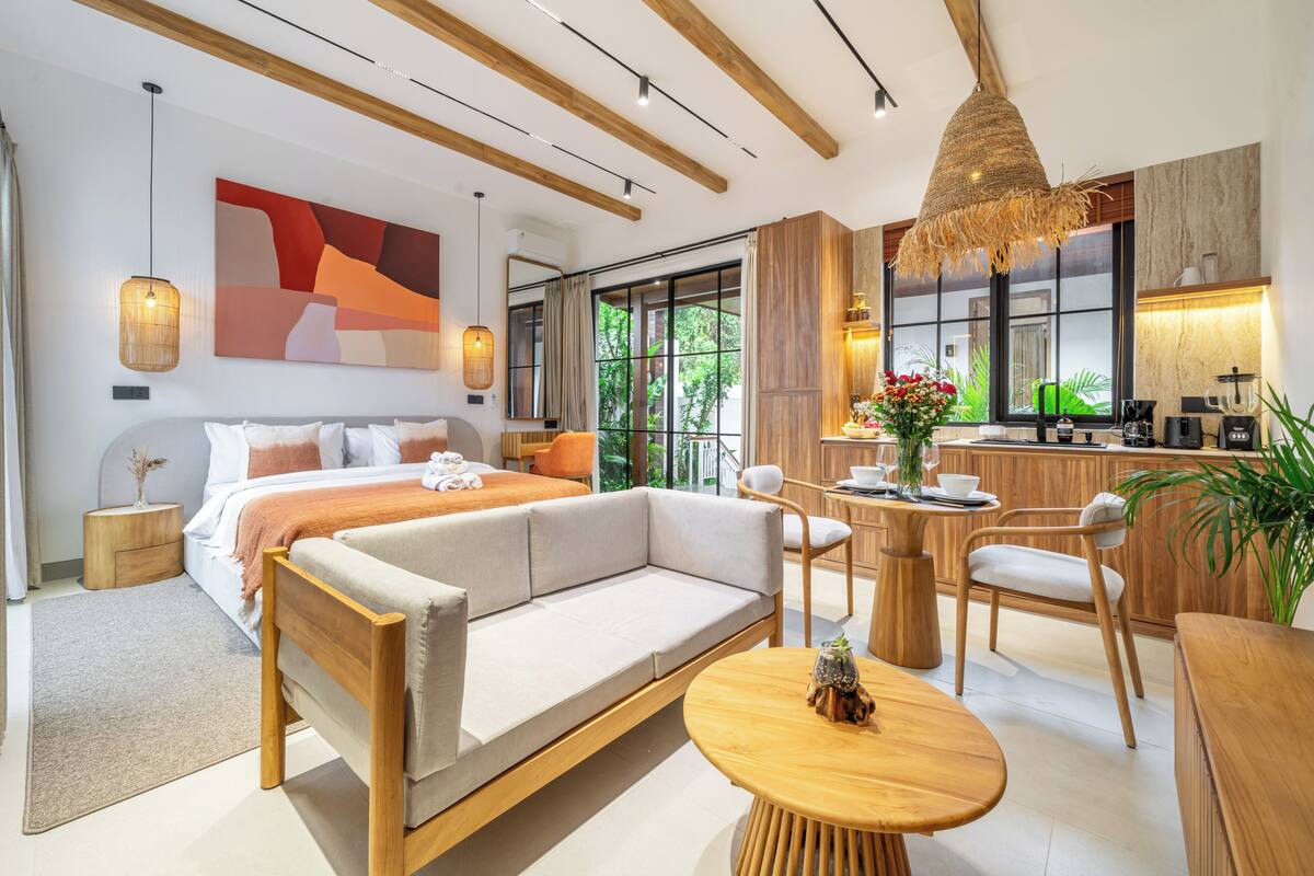 A modern bedroom with a sofa bed, a dining area with a round table, and a kitchen area with a bar.