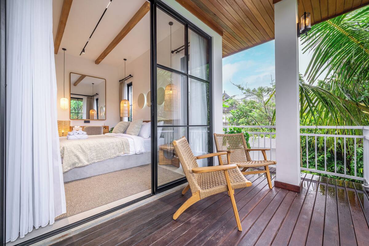A bedroom with a bed, a large window, and a balcony with wicker chairs.