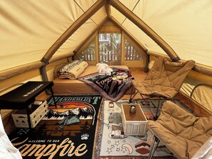 A tent with a bed, a blanket, a chair, a small table, and a wall-mounted heater.