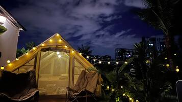 Una carpa con luces de cuerda, una silla y una mesa en una terraza de madera con palmeras.