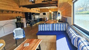 Een interieur van een blokhut met houten plafond, een eethoek en een zithoek met uitzicht op het water.