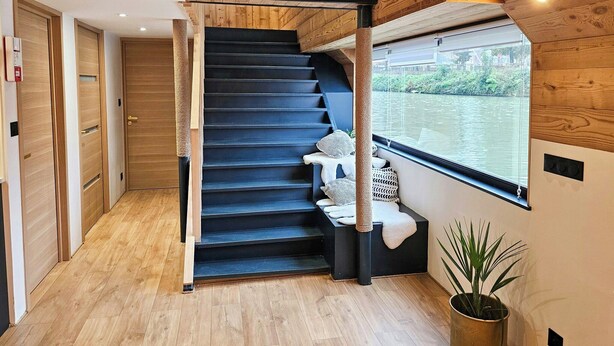 Een houten interieur met een trap die leidt naar een raam met uitzicht op een rivier.
