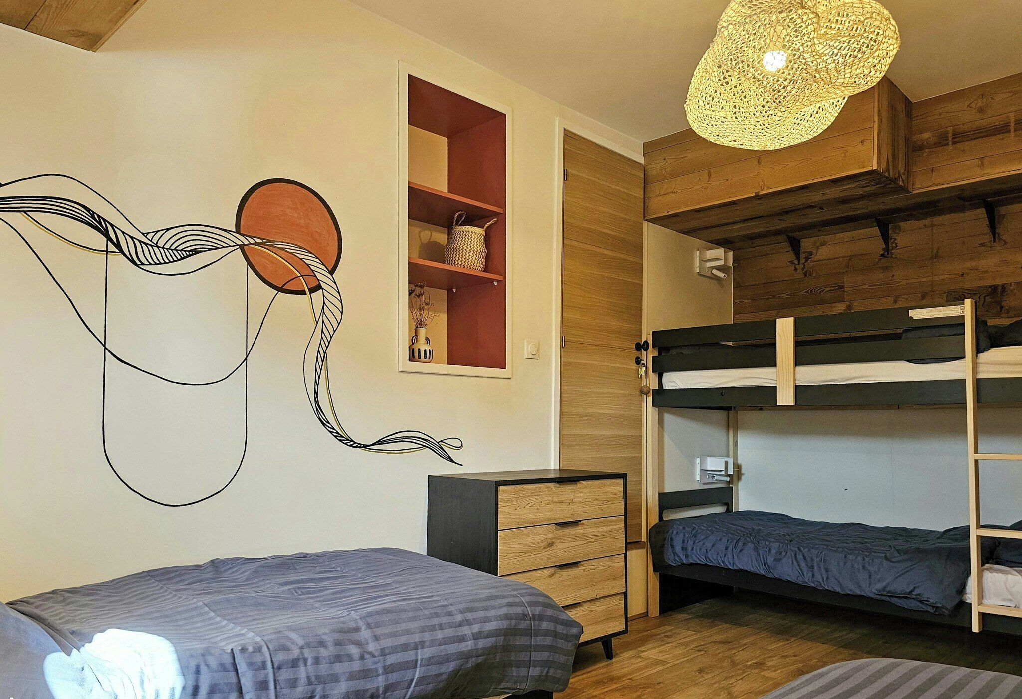 Een kamer met stapelbedden, een houten plafond, een kunstwerk aan de muur en een hanglamp.