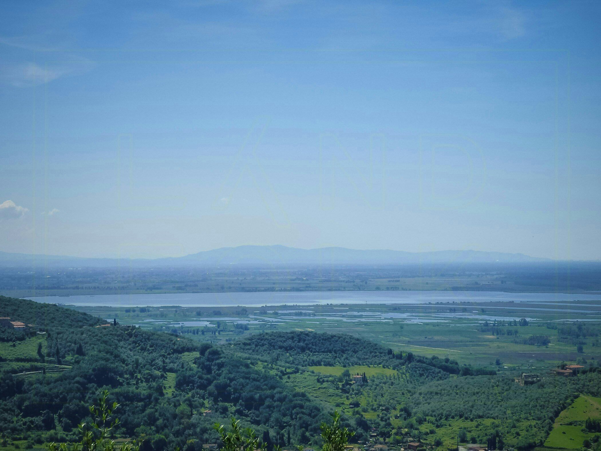 A panoramic view of a landscape with a river, hills, and scattered buildings.