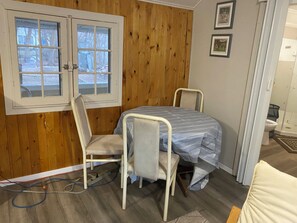 Une pièce avec un mur lambrissé en bois, une fenêtre, un lit recouvert d’une courtepointe à rayures, deux chaises et une petite table.