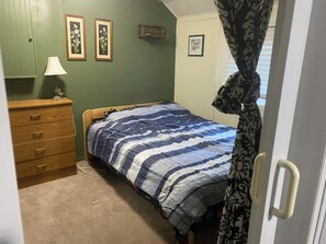A bedroom with a bed, a dresser, a lamp, and a door with a curtain. - 3 bedrooms cabin for rent (Sandy Hook)