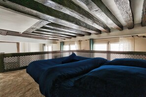 Ein Zimmer mit einem Bett, Holzbalken, einem Gitterkopfteil und Fenstern mit Vorhängen.