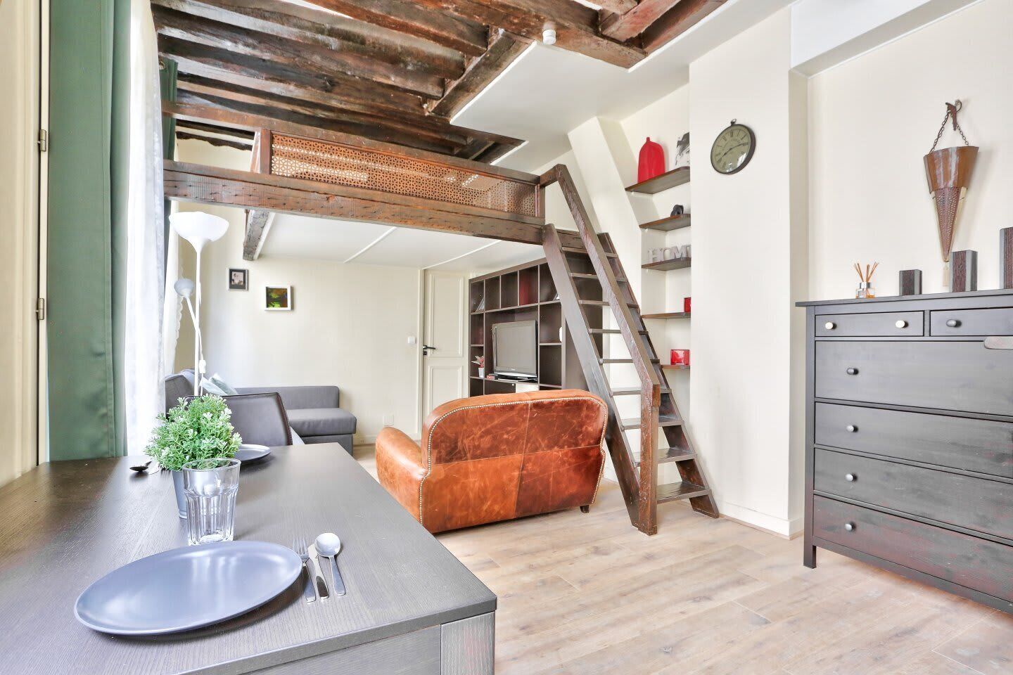 A modern living room with a loft bed, a dining area with a table set for two, and a staircase leading to a loft.